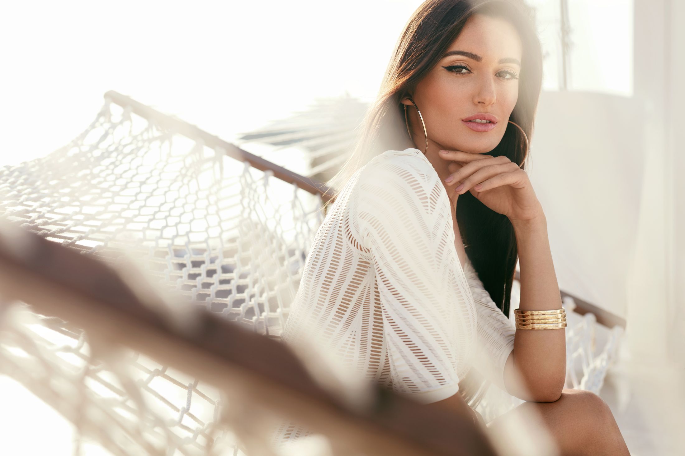 Woman relaxing in a hammock, sunlight backdrop.