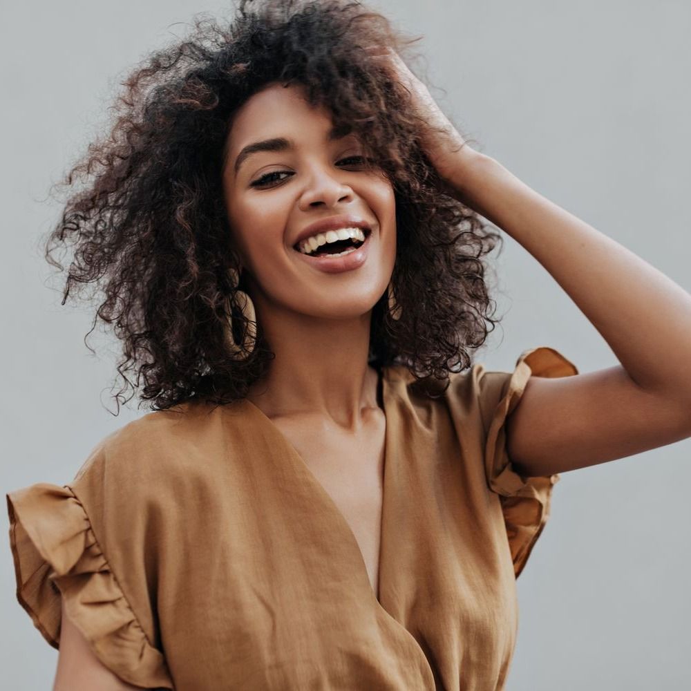 medspa patient model in a light brown top smiling and running her fingers in her hair