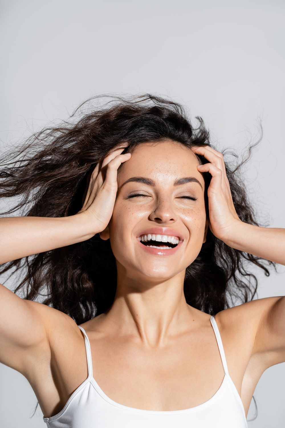 microneedling patient model in a white tank top with her hands on her temple and smiling