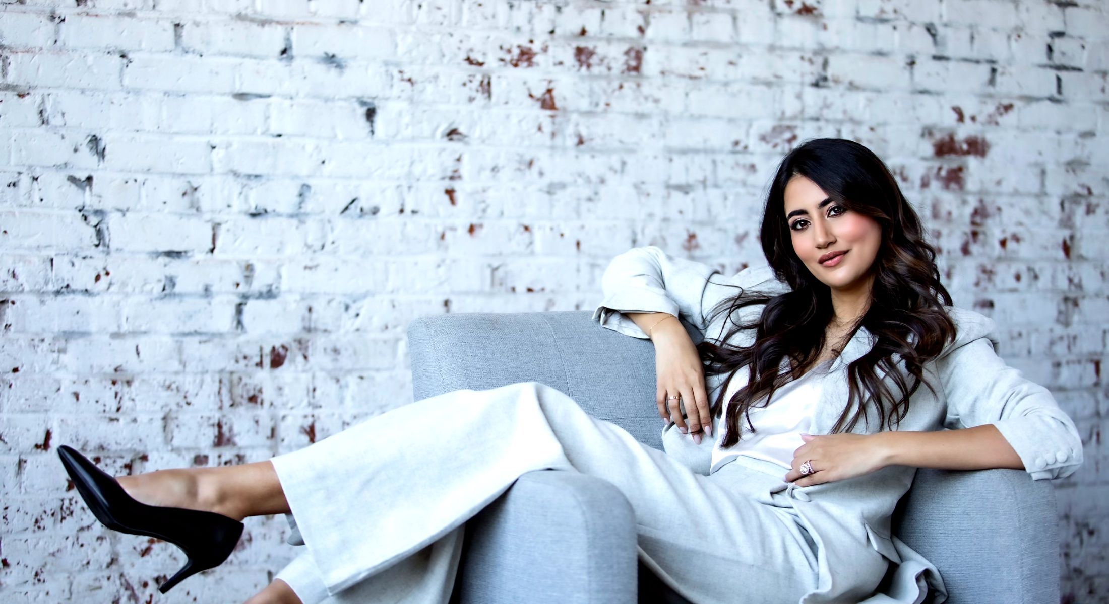 Karishma Lakhani reclining in a chair wearing a light gray suit